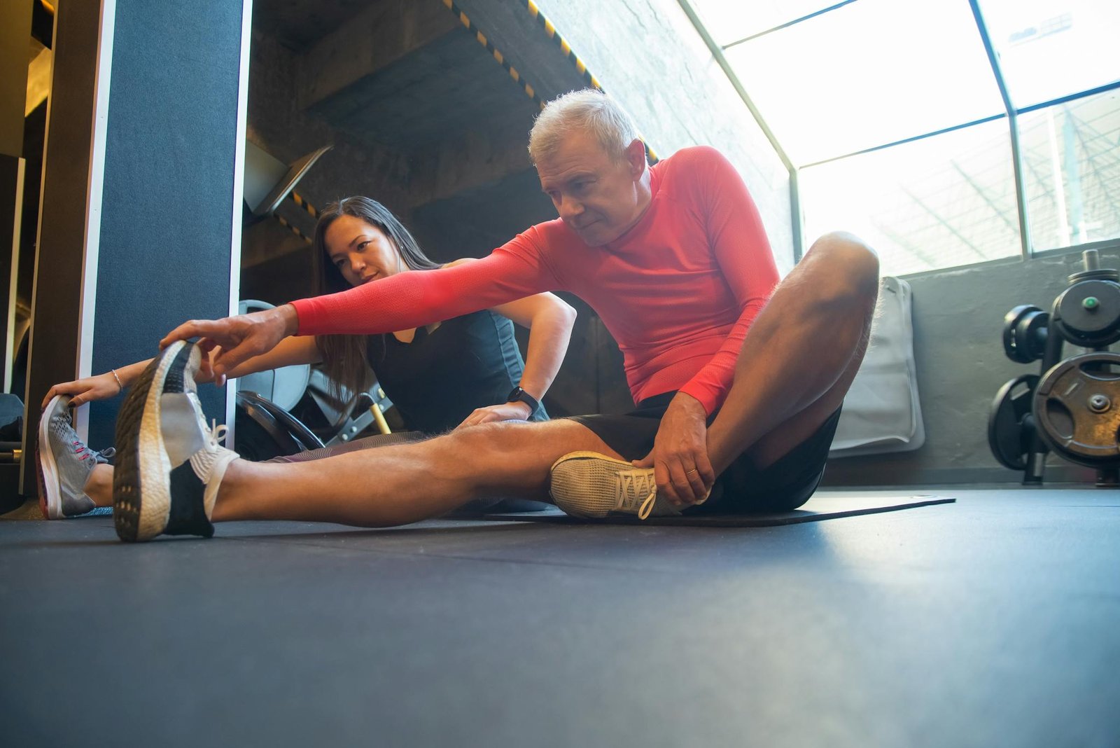 An elderly man stretches with a trainer